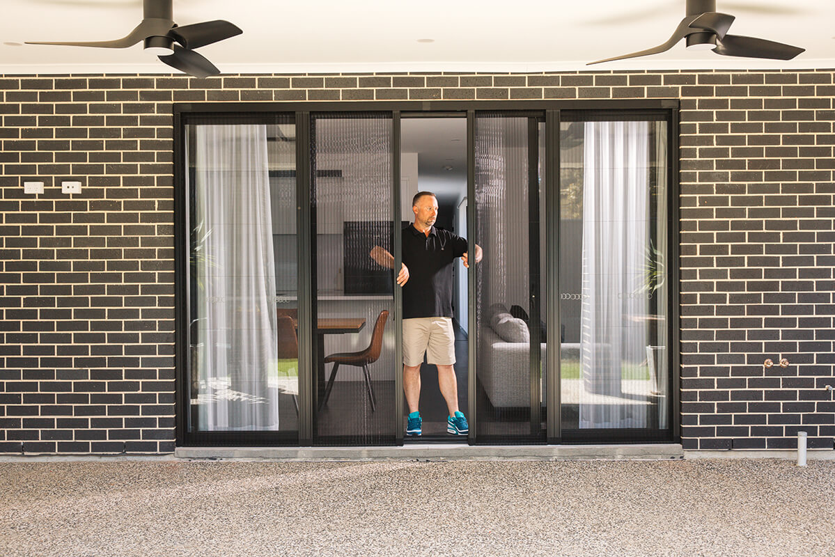 Man adjusting sliding glass doors with retractable black mesh screens.