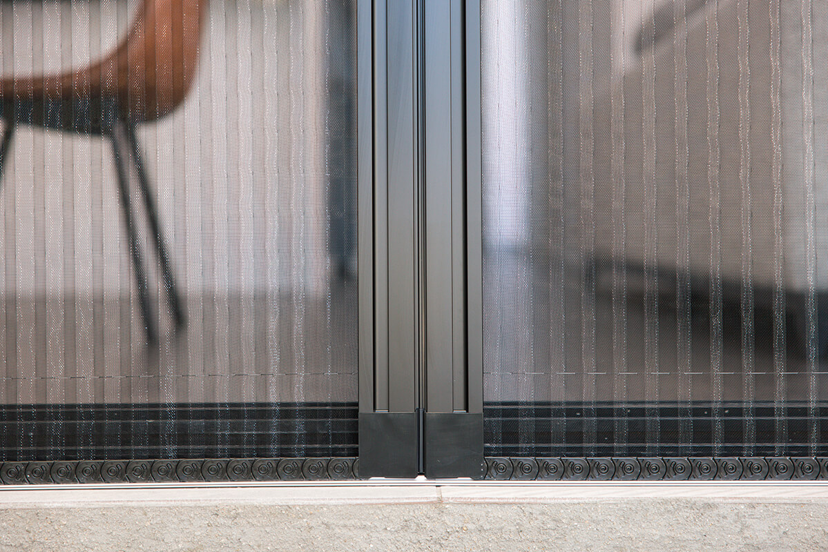 Dark gray retractable screen door with a textured bottom edge, installed on a concrete floor.