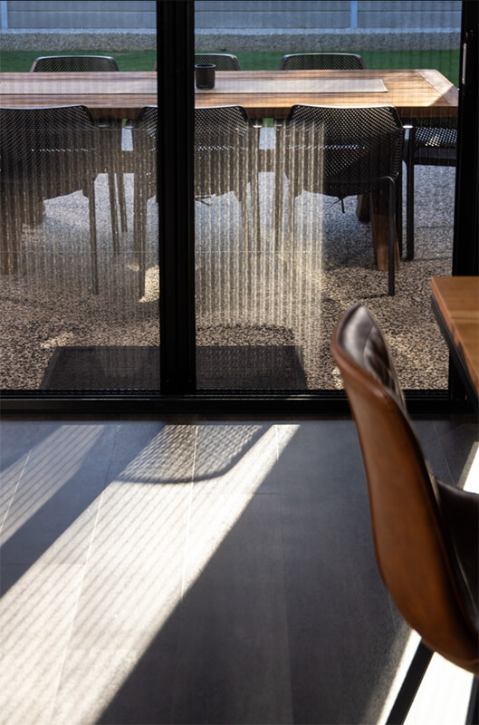 Exterior patio dining area viewed through a glass sliding door with patterned privacy film, showing a wooden table and chairs.