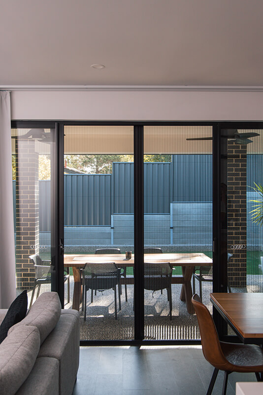 Modern living room with sliding glass doors showcasing a backyard patio dining area with a wooden table and chairs.