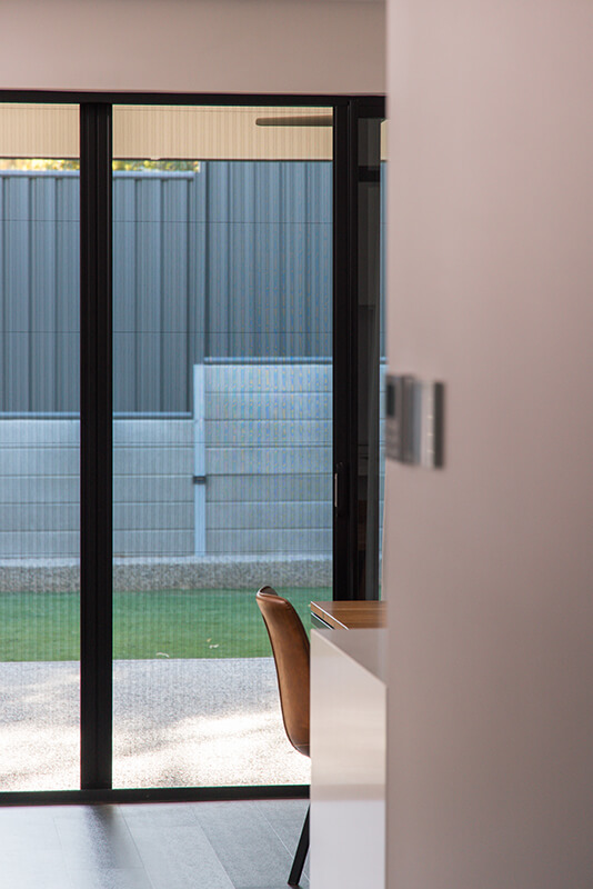 Modern interior with sliding glass doors to a backyard with a light-beige wall, a gray fence, and a light-brown chair.