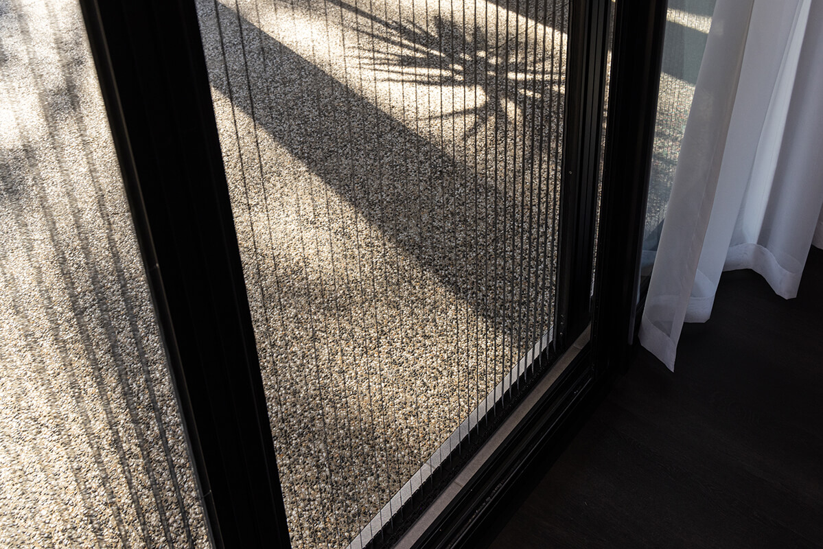 Sliding glass door with a retractable metal screen, showing shadows of a palm tree on a gravel patio.