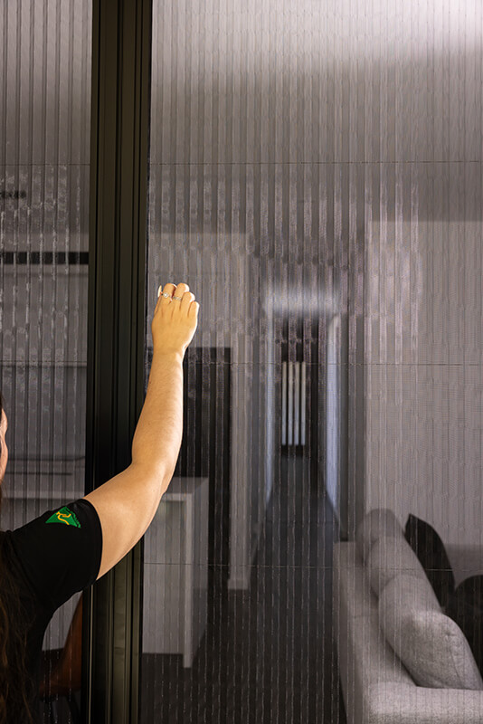 Person adjusting a vertical slatted window screen.
