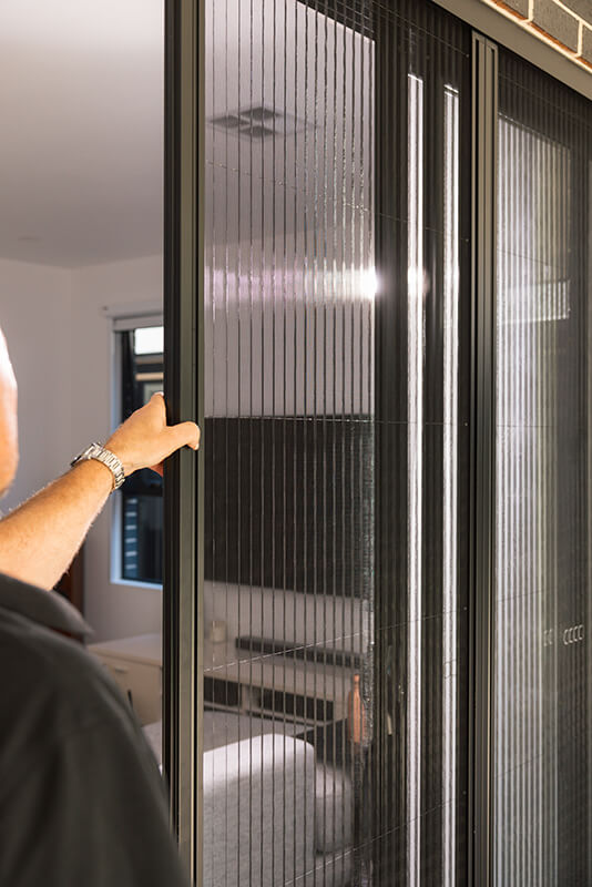 Person adjusting a vertical slatted window screen.