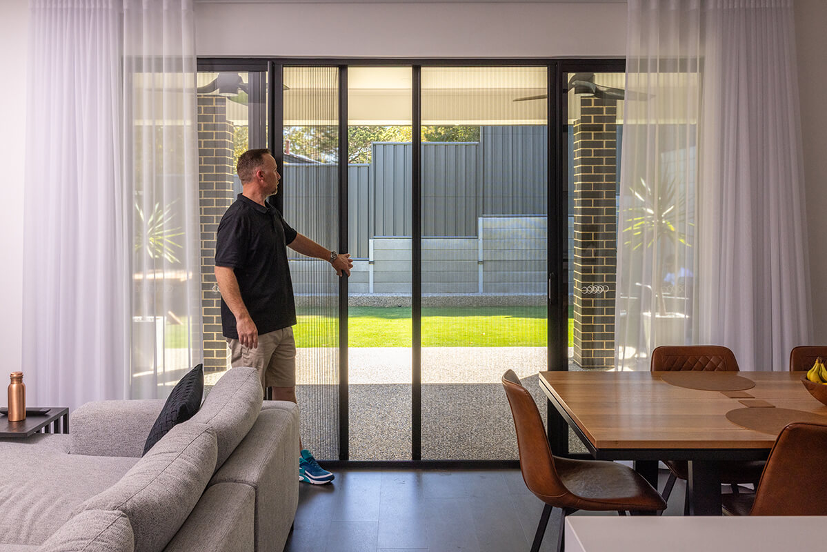 Person adjusting a vertical slatted window screen.