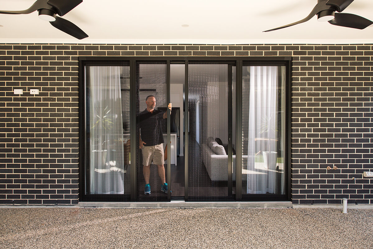 Person adjusting a vertical slatted window screen.