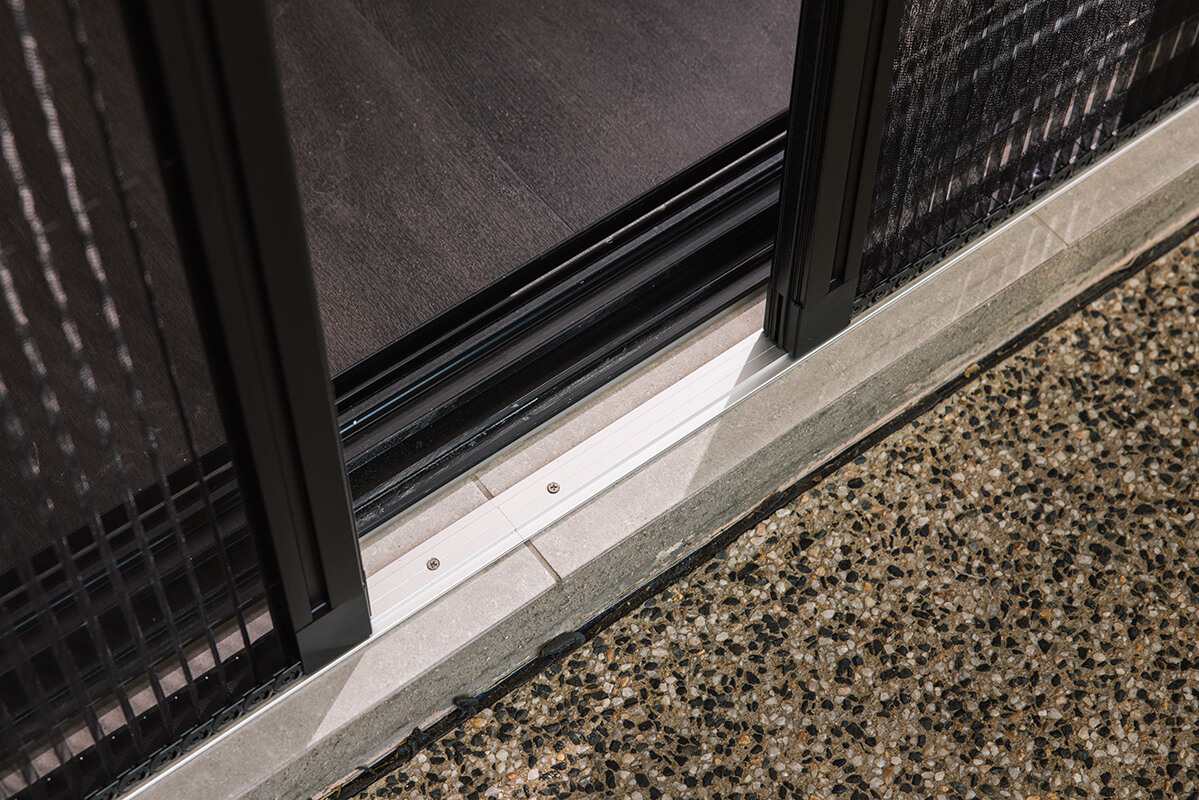 Close-up of a black sliding glass door with a retractable screen, showing the aluminum threshold and outdoor stone patio.