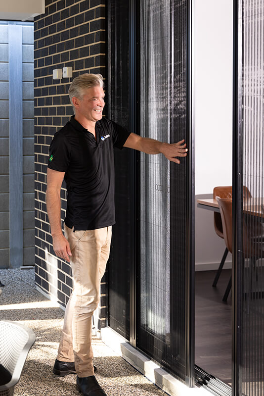 Person adjusting a vertical slatted window screen.