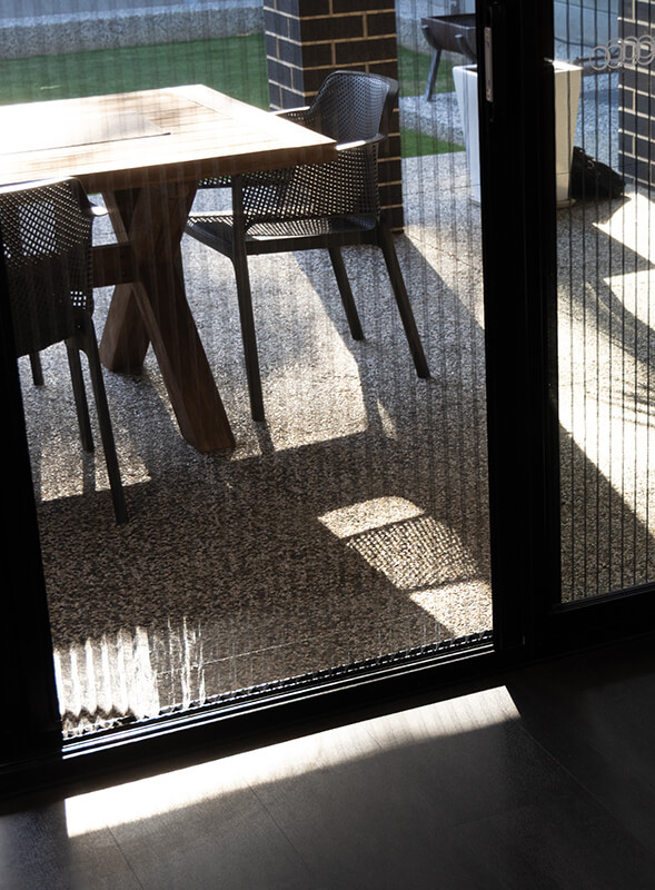 Outdoor dining area with a wooden table and black chairs, seen through a modern retractable screen door.